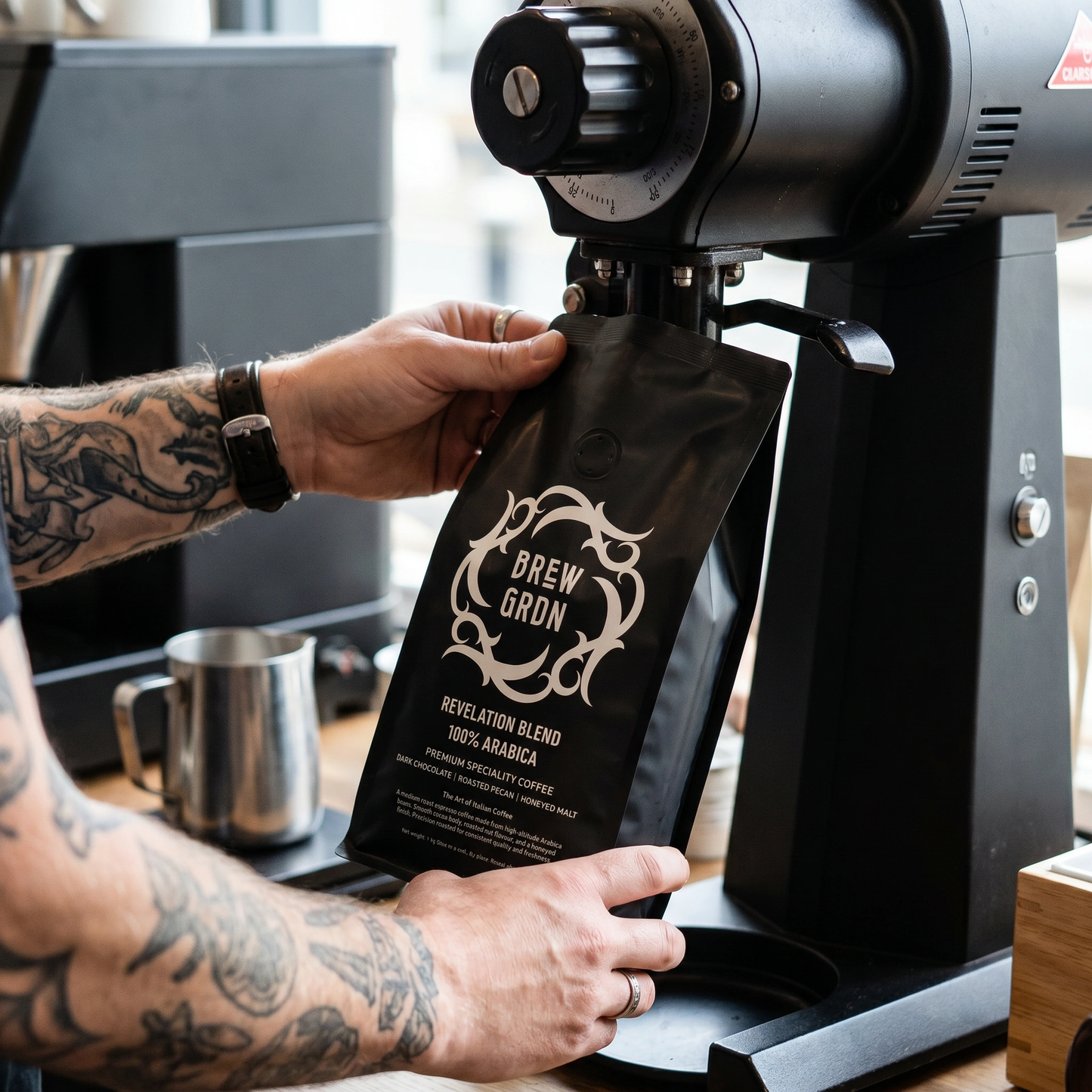 Person holding a coffee bag labeled 'Brew Gran' with a coffee grinder in the background.
