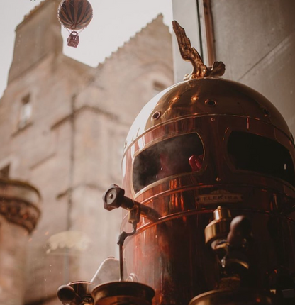Close-up of a large, ornate brass helmet with intricate details against a blurred architectural background.