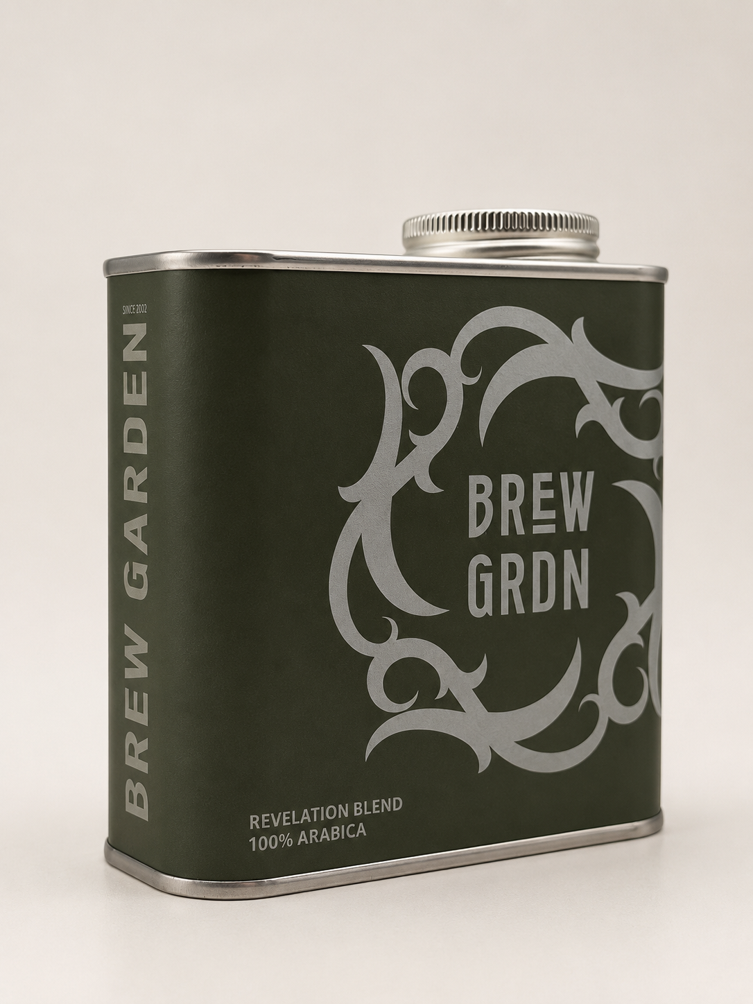 A rectangular metal coffee canister from Brew Garden in their Revelation Blend, featuring a dark olive green body with a silver ornate graphic and silver text, set against a plain light background.